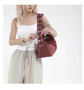 Detail of deep red shoulder bag featuring wide strap with large silver metal rivets