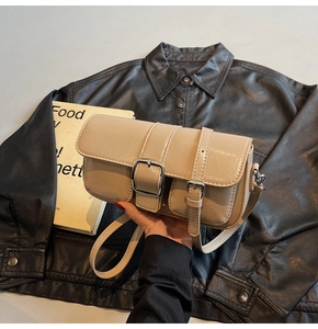 Detail of beige vintage crossbody bag with silver buckle held against black leather jacket