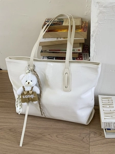 White crocodile pattern tote bag with bear charm on wooden floor with vintage books