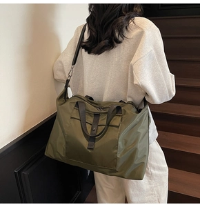 Olive green travel tote bag with flap pocket shown on a shoulder in a minimalist setting