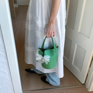 Detailed view of green litchi grain bucket bag with white flower charm held by a woman