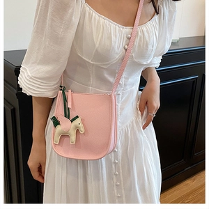 Detail of pink pebbled leather crossbody bag featuring a leather pegasus charm on model