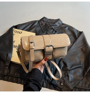 Detailed shot of beige patent leather crossbody bag with silver buckles and thin strap