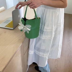 Detail view of grass green bucket bag with lychee grain texture and flower charm