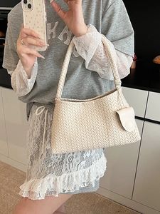 Minimalist cream woven shoulder bag with small circular charm pouch in a modern setting