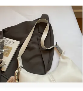 Close-up of white crossbody dumpling bag with soft stitching and plush ball charm