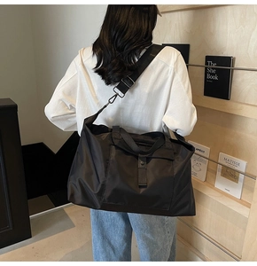 Detail of a large black nylon travel bag with adjustable strap worn by a person