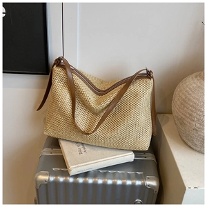 Gros plan du sac cabas en paille tressée avec lanières en cuir marron sur une valise