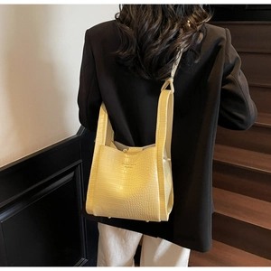 Detail of light yellow crocodile pattern bucket bag styled with a modern outfit