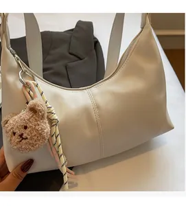 Detail view of cream leather shoulder bag with plush bear charm and woven cord detail