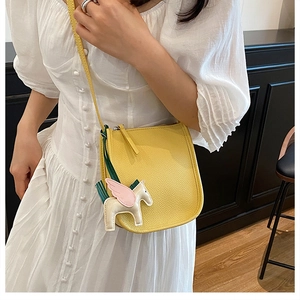 Detail of yellow pebbled leather crossbody bucket bag with white Pegasus charm on a model