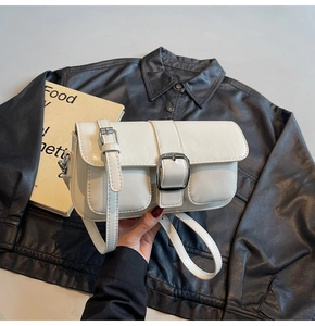 Detail of a chic cream-white crossbody bag with large silver buckle and front pockets
