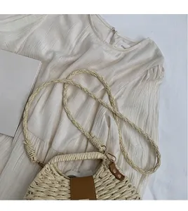 Detail view of woven straw beach bag with brown leather clasp and cream fabric background