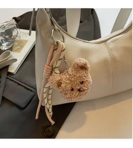 Detail of plush bear charm with colorful braided ropes on beige dumpling shoulder bag