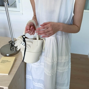 Close-up of white lychee leather bucket bag with floral charm and FUOR ribbon detail