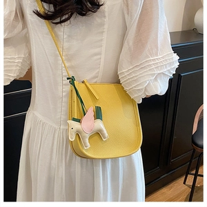 Detail of yellow lychee leather saddle bag with pegasus charm on a white dress