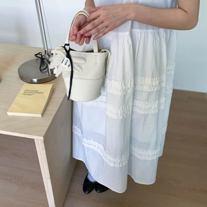 Close-up of white lychee textured bucket bag with decorative floral pendant and black ribbon
