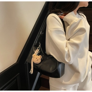 Detail of black faux leather shoulder bag with cute brown bear plush pendant and metal zipper