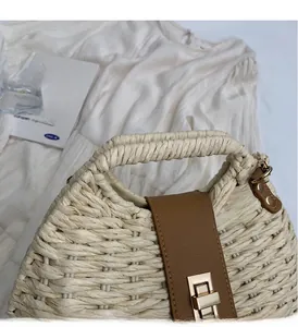 Close-up of woven straw handbag featuring brown leather strap and gold swivel lock detail
