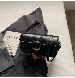 Detail of a black glossy leather crossbody bag with a silver buckle on a white bed
