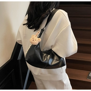 Detail of a black faux leather hobo shoulder bag with a cute plush bear charm accessory