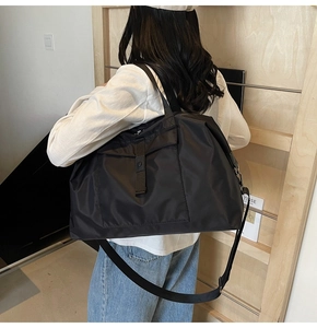 Detailed side view of black nylon travel bag with shoulder strap worn by a model