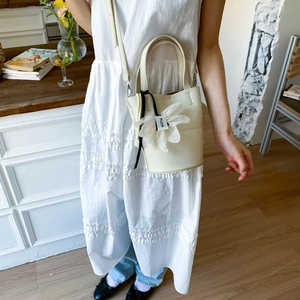 Detail of off-white lychee grain leather bucket bag with a floral charm and sturdy handle