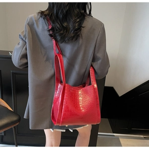 Detailed view of red crocodile-patterned bucket bag shown on a model in a modern interior