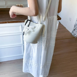 Detail of white lychee leather bucket bag with floral charm and slim shoulder strap