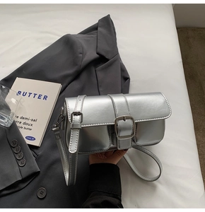 Silver metallic crossbody bag on white bedding with modern lifestyle accessories