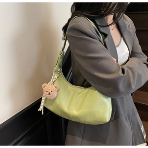 Close-up of avocado green pleated shoulder bag with a cute brown plush bear charm