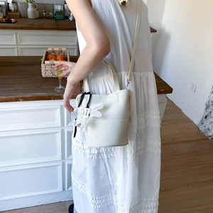 Detail of white lychee grain leather bucket bag featuring a fabric flower charm and long strap