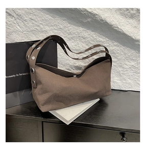 Detail view of brown suede shoulder bag with silver grommets on the wide strap
