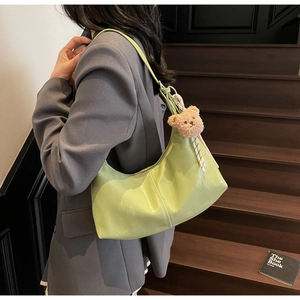 Detail of avocado green hobo bag with plush bear charm and striped strap on model