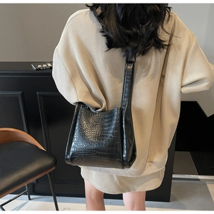 Detail of black crocodile texture bucket bag with gold metal feet and glossy leather