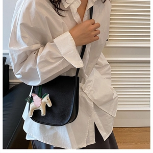 Detail of a black leather saddle bag with a pony charm worn by a model in a white shirt