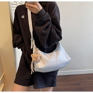 Detailed view of cream crescent crossbody bag with brown plush bear charm and adjustable strap