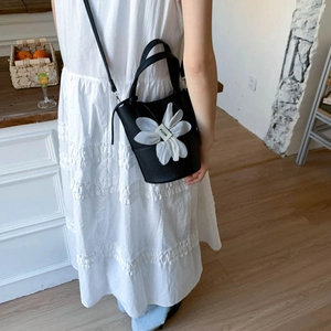 Detail of black lychee texture bucket bag with large white fabric flower and strap