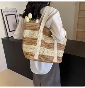 Detailed view of a woven straw tote bag with brown stripes and white fabric straps