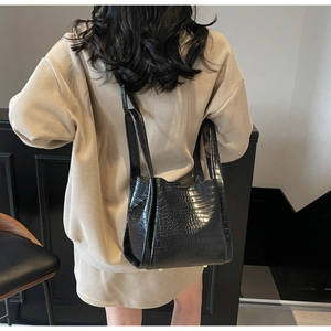 Close-up of black crocodile pattern leather bucket bag held by a model in beige outfit