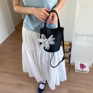 Black pebbled leather bucket bag with white mesh flower charm on a model's shoulder