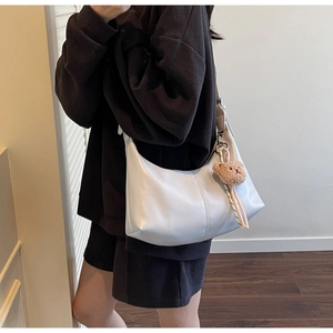 Detail view of a white crescent shoulder bag featuring a cute brown plush bear pendant