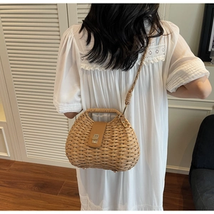 Detail of woven straw bag showing brown leather flap, gold metal lock, and top handle
