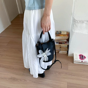 Detail of black lychee grain leather mini bucket bag with a white organza flower charm