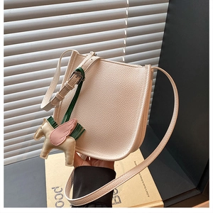 Detail of a beige pebbled leather saddle bag with a decorative pegasus charm accessory