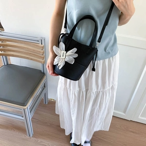 Fashionable black bucket bag with a large white gauze flower detail and crossbody strap