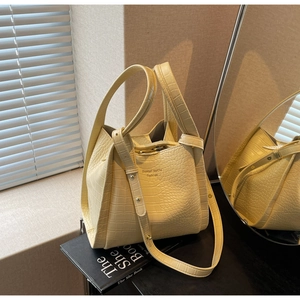 Detail showing crocodile texture leather, adjustable strap and gold logo on yellow bucket bag