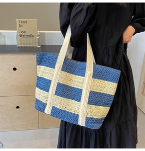 Close-up of blue and white striped straw tote bag with wide handles shown on shoulder