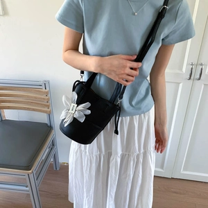Detail of black lychee grain bucket bag with white floral charm worn on shoulder