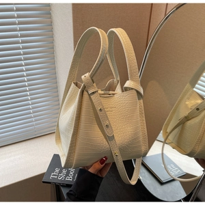 Detail of cream faux crocodile bucket bag with double handles and adjustable strap in a mirror
